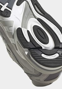 Atletska cipela siva i crna, s teksturiranim gumenim đonom, utorima za fleksibilnost i detaljima brendiranja.