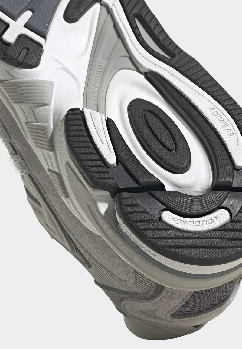 Suela de zapatilla deportiva en gris y negro, con un diseño de goma texturizada, ranuras para flexibilidad y detalles de marca.