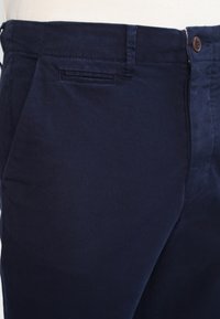 Marina blå bomullsbyxor med en smidig textur, med en framficka, diskreta sömmar och knäppning med knapp.