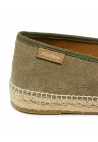 Close-up van een olijfgroene canvas espadrille met gevlochten jute zool en een 'Finsbury' stoffen label aan de zijkant.