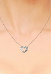 Collana d'argento con pendente a forma di cuore, caratterizzata da un centro vuoto e circondata da piccoli gemme trasparenti. La catena è delicata e finemente collegata.