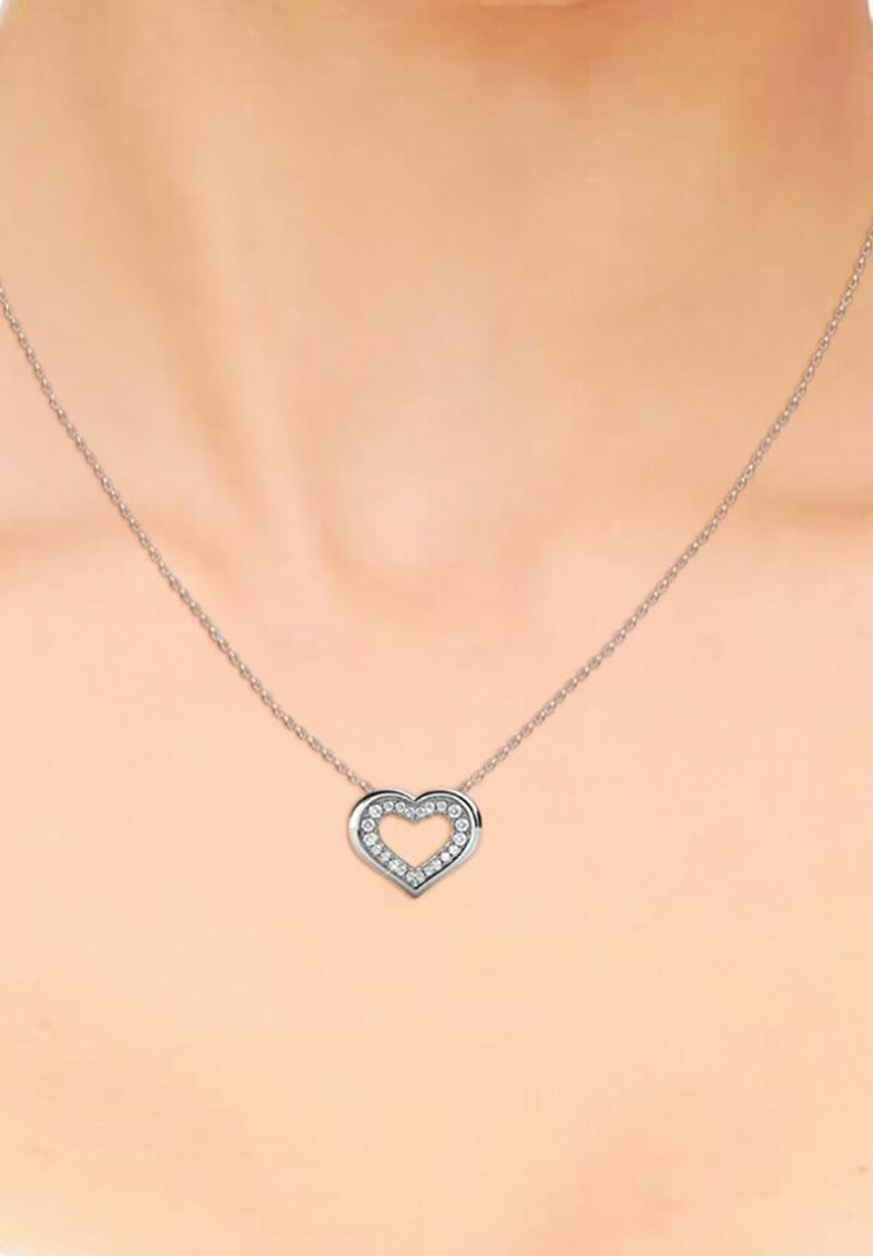 Collana d'argento con pendente a forma di cuore, caratterizzata da un centro vuoto e circondata da piccoli gemme trasparenti. La catena è delicata e finemente collegata.