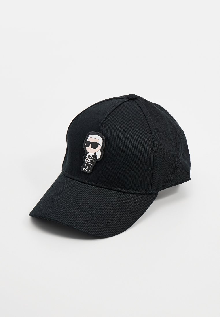 Gorra de béisbol negra con tejido texturizado, visera curvada y un pin de personaje de dibujos animados con gafas de sol en la parte frontal.