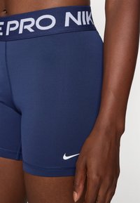 Nike Pro shorts i marineblå, med en bred elastisk talje med "NIKE PRO" i hvid, glat tekstur og et lille hvidt logo på siden.