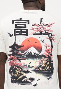 Witte t-shirt met een kleurrafische afbeelding van kersenbloesems, een berg en een pagode, met zwarte en rode accenten. Chinese karakters zijn inbegrepen.