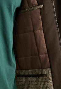 Roheline sviiter ja pruun jakki, millel on tikitud pruun vooder. Omab tekstureeritud villakangast mustrit ja tõmblukku; sisaldab tasku detaili.