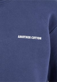 Námornícky bavlnený sveter s bielym textom "ANOTHER COTTON" na prednej strane, so sviežou textúrou a klasickým okrúhlym výstrihom.