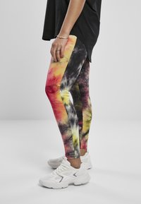 Fargerike tie-dye leggings med røde, gule og svarte mønstre, kombinert med hvite sportssko og en svart oversized topp.