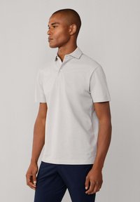 Polo de color gris claro hecho de tela suave, con cuello, mangas cortas y un solo botón como detalle. Diseño limpio sin patrones visibles.