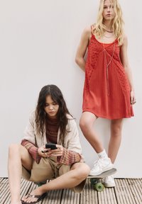 Due modelle presentano abbigliamento: una indossa un vestito rosso senza maniche con dettagli ricamati, l'altra indossa un maglione multicolore, pantaloni corti e sandali.