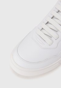Sneaker bianco in pelle con superficie liscia, lacci bianchi piatti e punta arrotondata. Presenta cuciture sui lati e una suola in gomma testurizzata.