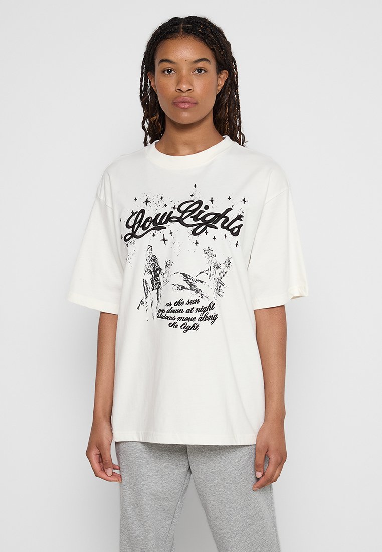 T-shirt en coton blanc avec impression graphique noire, présentant les mots "Glow Lights" et des illustrations de la nature, coupe ample et manches courtes.