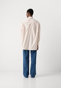 Camicia a righe color crema con una vestibilità rilassata, dettaglio della piega sul retro e maniche lunghe, abbinata a pantaloni di denim blu larghi.