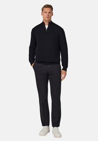 Czarny sweter dzianinowy z kołnierzykiem na pół-zamek, zestawiony z ciemnymi spodniami i białymi trampkami. Czyste linie i teksturowana tkanina.