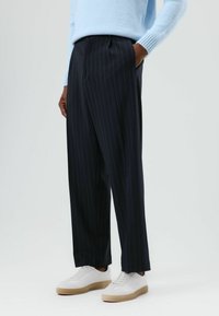 Marineblauwe broek met krijtstrepen gemaakt van een gladde stof, met een losse pasvorm en zijzakken, gecombineerd met witte sneakers en een lichtblauwe trui.