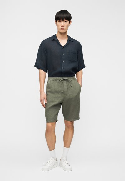 Chemise en lin bleu foncé à manches courtes avec poche avant, associée à un short en lin vert olive avec ceinture élastique et poches latérales.