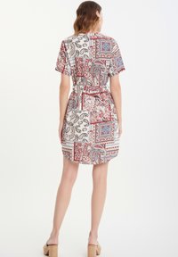 Korte mouw jurk in een patchwork ontwerp, met paisley en geometrische patronen in rood, blauw en crèmekleur, met een ceintuur in de taille.