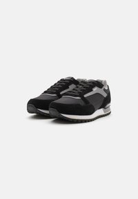 Zapatos deportivos negros con una combinación de materiales sintéticos y de ante. Presentan acentos grises, texturas contrastantes, cordones redondos y una suela texturizada.