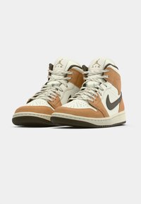 Fehér, bézs velúrból és barnából készült magas szárú Nike Air Jordan sneaker, szögletes oldalnézetben, megkötött fűzőkkel és a Jumpman logóval a nyelvén.