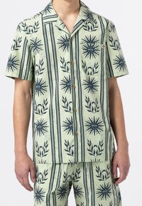 Kortsleeved kragskjorta i ljusgrön tyg med marinblå punktmönster och bladmotiv, med en bröstficka och knappar av trä.