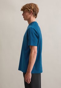 Krótki rękaw, t-shirt z okrągłym dekoltem wykonany z gładkiej bawełny w kolorze morskim, charakteryzujący się luźnym krojem i subtelnymi detalami szwów na ramionach i łączeniach.