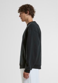 Schwarzer Langarm-Sweatshirt mit lockerer Passform, featuring gerippte Bündchen und Saum sowie einer weichen Textur. Auf einem Modell im Profil gezeigt.