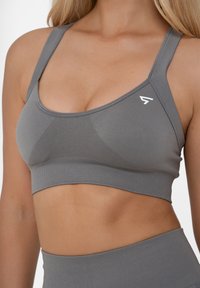 Grijze sportbeha met brede bandjes, textuurpanelen en een klein wit logo dat het ontwerp accentueert. Zacht, rekbaar materiaal dat zich aan het lichaam aanpast.