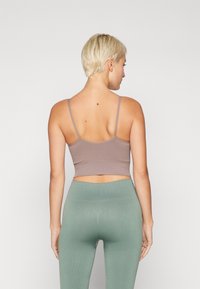 Šokolādes brūns ribotu crop top ar plānām siksnām, kombinēts ar augsta vidukļa piparmētras zaļām legingām, kas izceļ gludu tekstūru un piegulšanu.