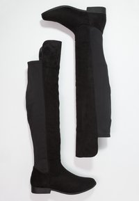 Botas negras por encima de la rodilla que combinan ante y tela lisa, con tacón plano y un diseño elegante y ajustado.