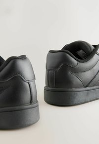 Baskets noires avec une tige en cuir lisse, un col rembourré et une semelle en caoutchouc texturé. Design minimaliste avec des détails de couture subtils.