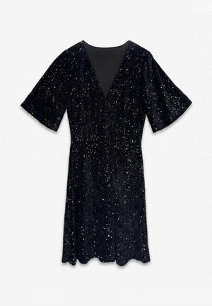 Robe noire longueur genou ornée de sequins scintillants, avec des manches courtes évasées et un empiècement transparent en V au niveau de l’encolure, sur fond blanc.