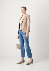 Beige upravený blazer s jedním knoflíkem, kombinovaný s světle modrými rovnými džíny, olivově zelenými lodičkami s špičatou špičkou a malou kabelkou.