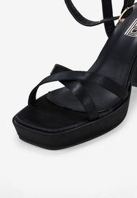 Sandalias de plataforma negras con tiras cruzadas de satén, punta cuadrada y un tacón grueso. Textura suave con un diseño minimalista.