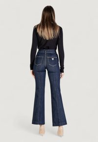 Jeans a vita alta svasati di colore blu scuro con due tasche posteriori e cuciture a contrasto, abbinati a un top nero a maniche lunghe.