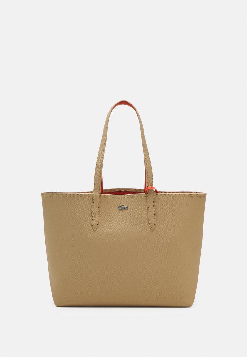 Saco tote bege com textura suave, duas alças e interior vermelho. Apresenta um pequeno logotipo prateado na frente. Design retangular simples.