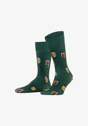Grüne Socken mit einem wiederholten Nussknacker-Design in Gelb, Rot und Schwarz. Das Material ist glatt mit gerippten Bündchen und mittlerer Höhe.