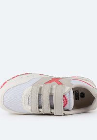 Zapatilla ligera con parte superior de malla blanca, detalles en ante beige, suela de goma rosa y tres correas de velcro. Presenta un logo rosa prominente.