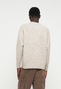 Light beige knitted sweater with a round neckline and raglan sleeves. Features a textured fabric and a straight hem. Worn with brown cargo pants.