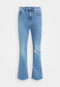 Jean évasé bleu clair en denim. Présente une déchirure usée sur le genou gauche. Design classique à cinq poches avec bouton en métal et fermeture éclair.