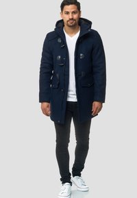 Abrigo de mezcla de lana en color navy con capucha, cierres de tipo toggle, dos bolsillos frontales y cremallera. Combinado con pantalones slim-fit negros y zapatillas blancas.