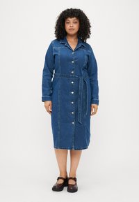 Vestido de ganga com colarinho, mangas longas e cintura apertada. Apresenta botões prateados à frente e um comprimento médio. Cor azul escura.