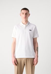 Korte mouwen witte polo met een klassieke kraag, voorzien van een logo op de kraag en een klein merkembleem op de borst. Gladde katoenstof.