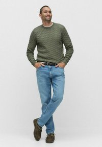 Olivgrön kabelstickad tröja, ljusblåjeans och bruna skor. Tröjan har rundad halsringning och strukturerat mönster. Avslappnad outfit.