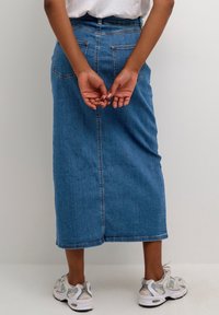 Falda midi de mezclilla en azul, con corte recto, bolsillos traseros y un dobladillo que cae por debajo de las rodillas, combinada con zapatillas blancas y plateadas.