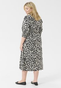 Midi-jurk in lichte stof met een zwart-beige luipaardprint. Gemaakt met lange mouwen en een getailleerde taille. Zwarte ballerina's.