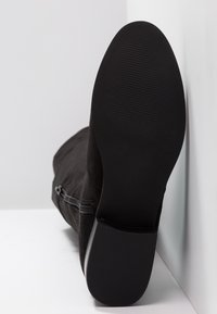Bottine en daim noir avec une semelle en caoutchouc lisse et plate et une fermeture éclair latérale, présentant un bout légèrement effilé et une tige texturée.