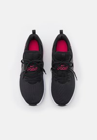 Zapatillas deportivas negras con parte superior texturizada, detalles en rosa y suela blanca. Diseño con cordones y marca destacada en los laterales y la lengüeta.