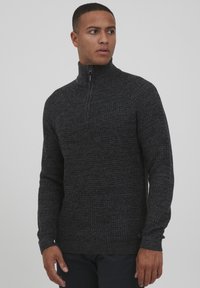 Dunkelgrauer Strickpullover mit hohem Kragen und Viertelreißverschluss, der ein strukturiertes Muster und gerippte Bündchen aufweist.