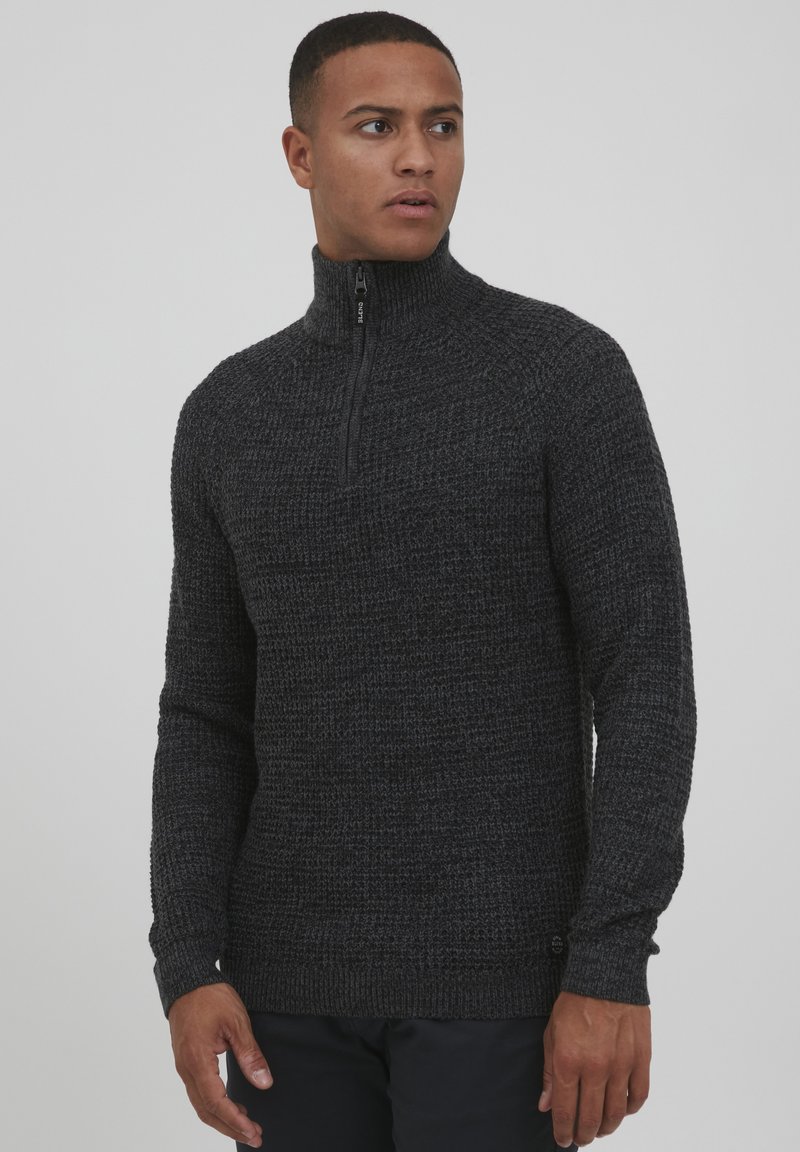 Dunkelgrauer Strickpullover mit hohem Kragen und Viertelreißverschluss, der ein strukturiertes Muster und gerippte Bündchen aufweist.