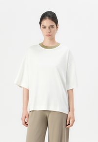 Witte oversized t-shirt met korte mouwen en een olijfgroen ronde hals. Zachte stof, losvallende pasvorm en recht afgebroken ontwerp.